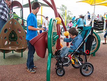 Two boys playing on a playground panel, one of whom is in a mobility device
