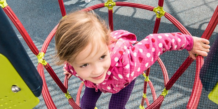 Girl climbing on a red climbing element on a Landscape Structures playground 
