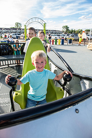 A little boy smiles into the camera while sitting on a lime green seat on a playground structure. 