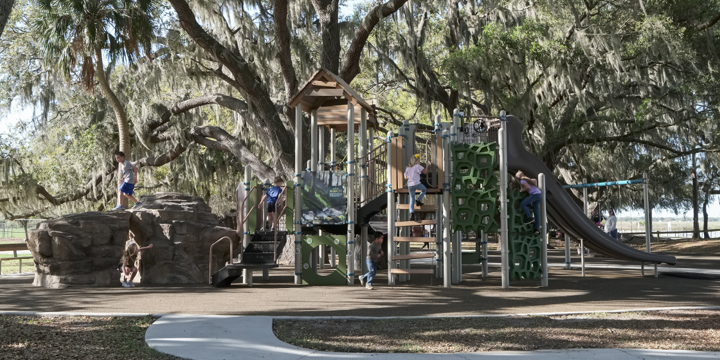 A light brown and bright green playground structure blends into the background of a huge, light brown tree and light brown surfacing. 